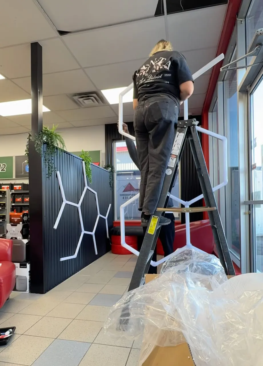 Installation des néons hexagonaux depuis un escabeau dans une salle d’attente