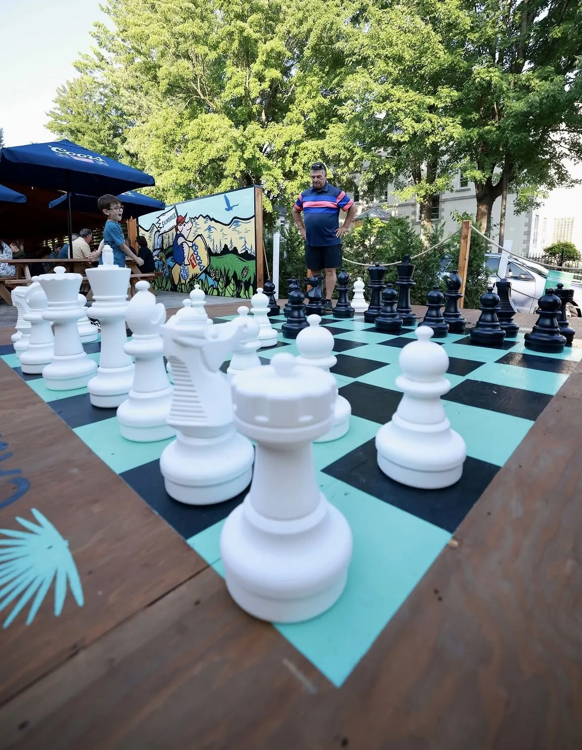 Pièces d’échecs géantes blanches et noires sur un damier en vinyle turquoise et noir, en terrasse