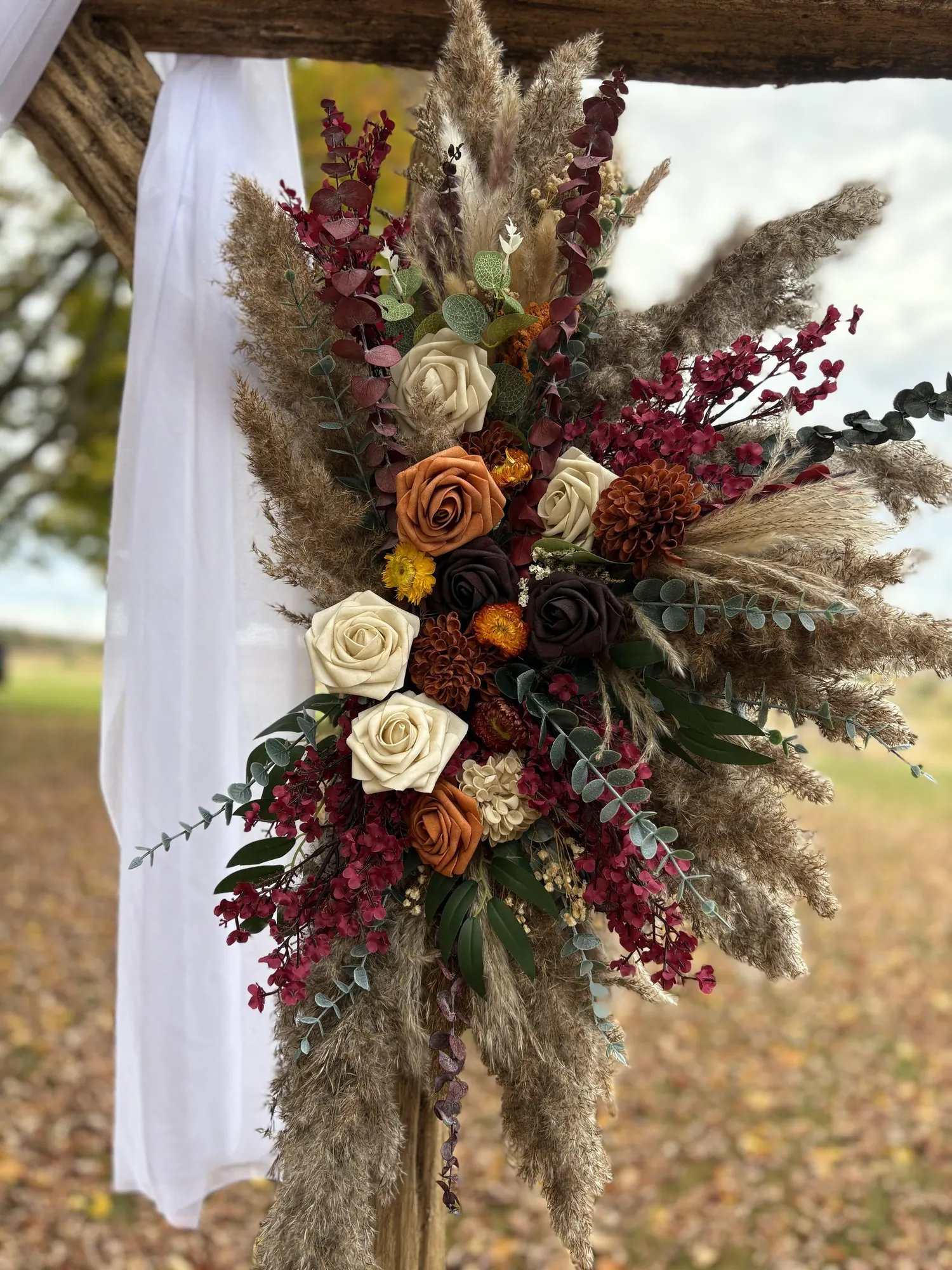 Bouquet de fleurs séchées aux teintes automnales accroché à l’arche de mariage