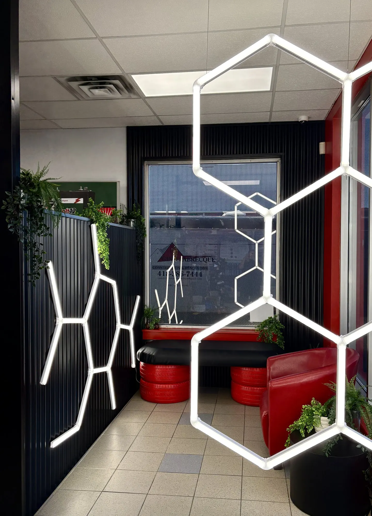 Salle d’attente réaménagée : demi-mur en tôle ondulée noire, néons hexagonaux et banquette en pneus rouges