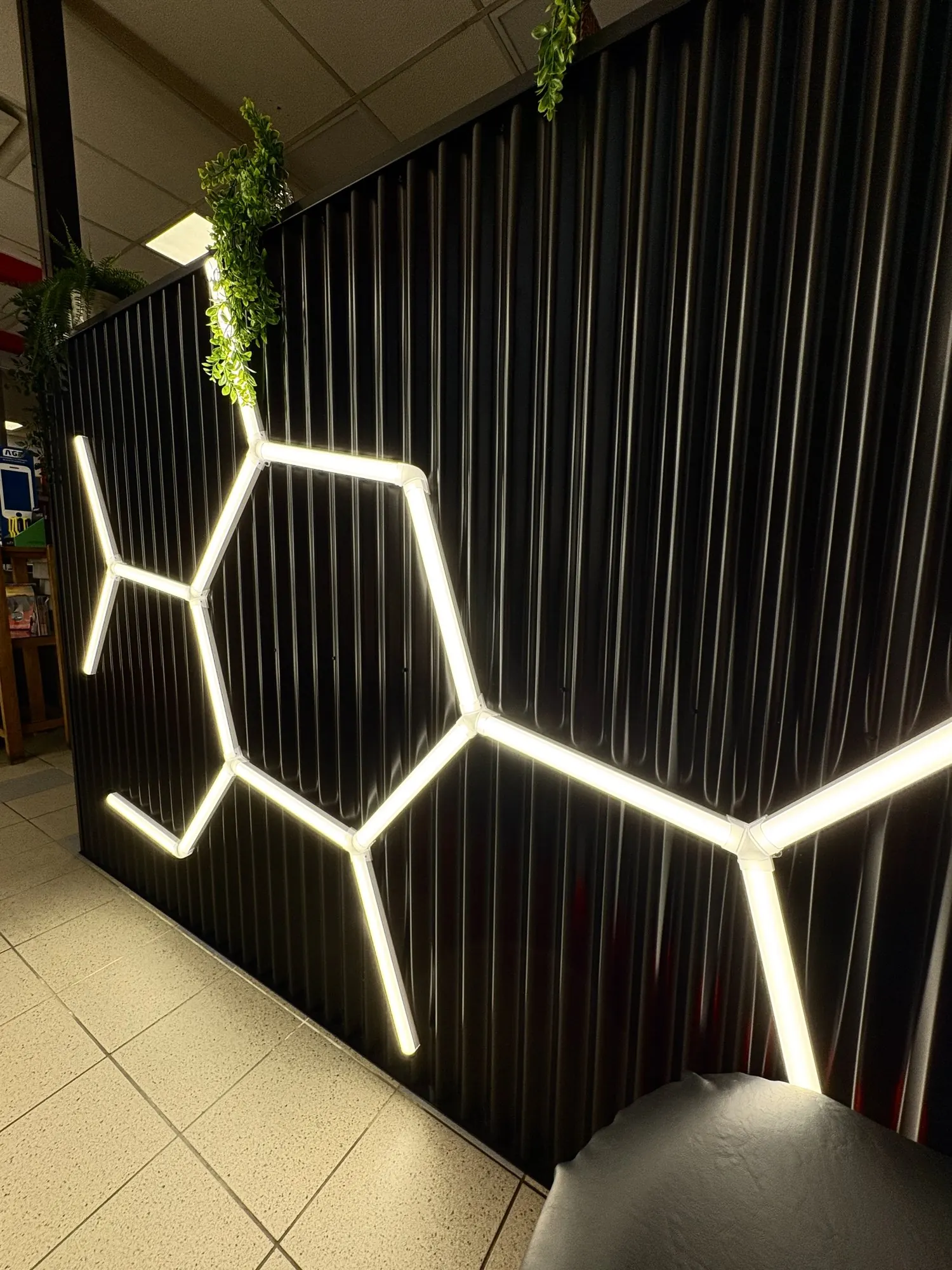 Néon blanc en forme d’alvéoles sur le demi-mur en tôle ondulée noire