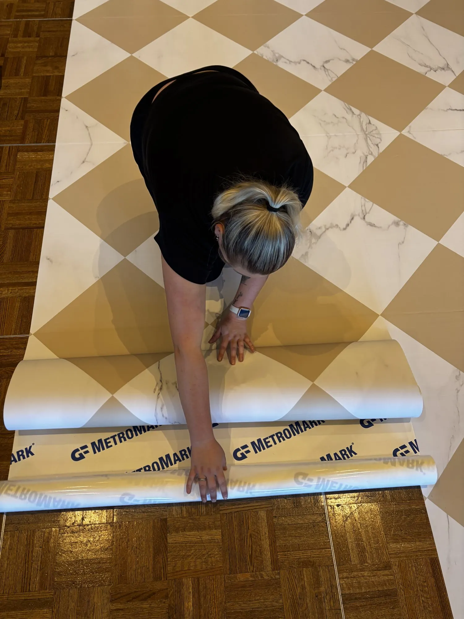 Esther déroulant un lé de vinyle en damier effet marbre sur le parquet