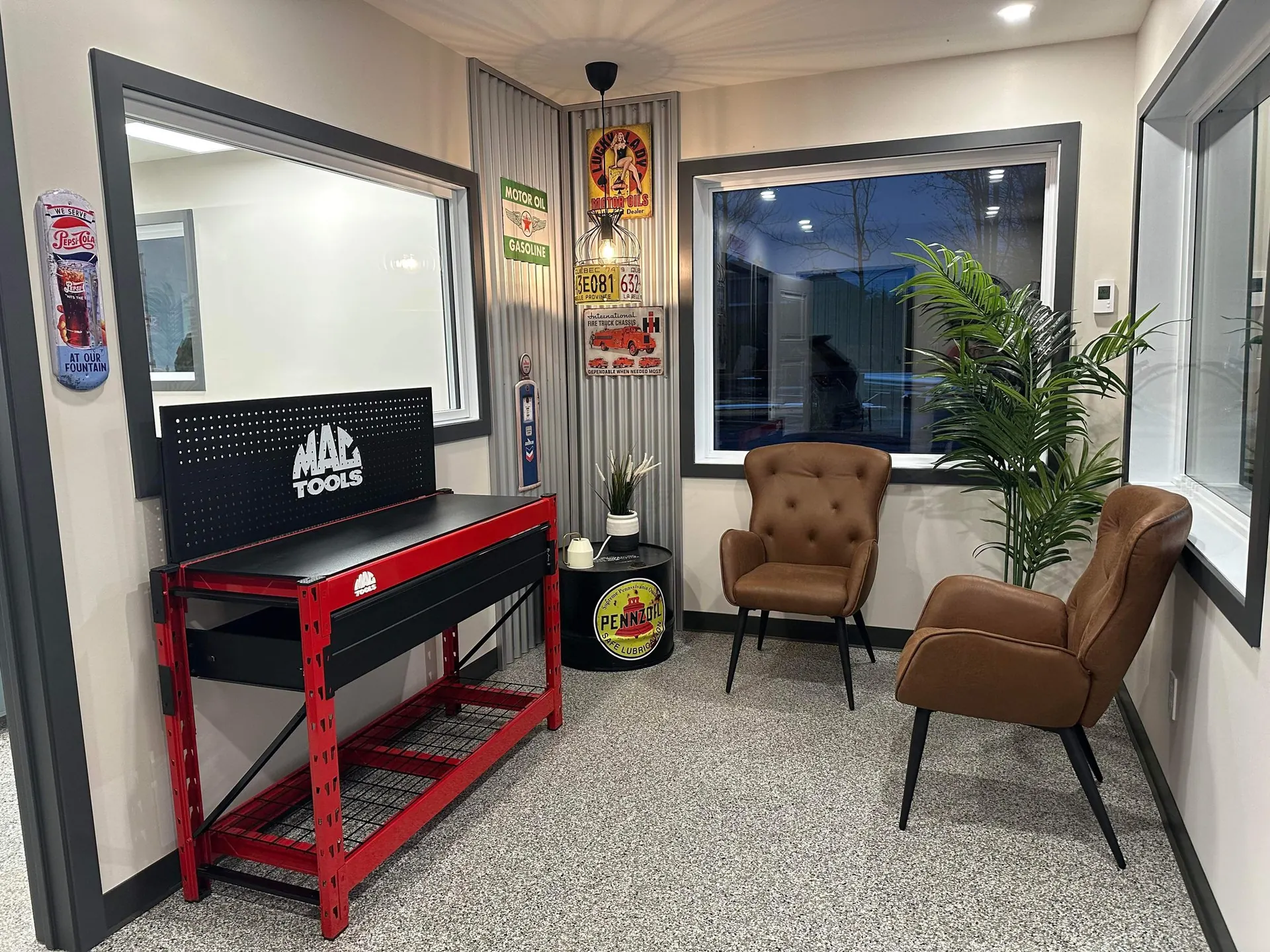 Salle d’attente au décor de garage avec établi rouge, fauteuils et plaques rétro