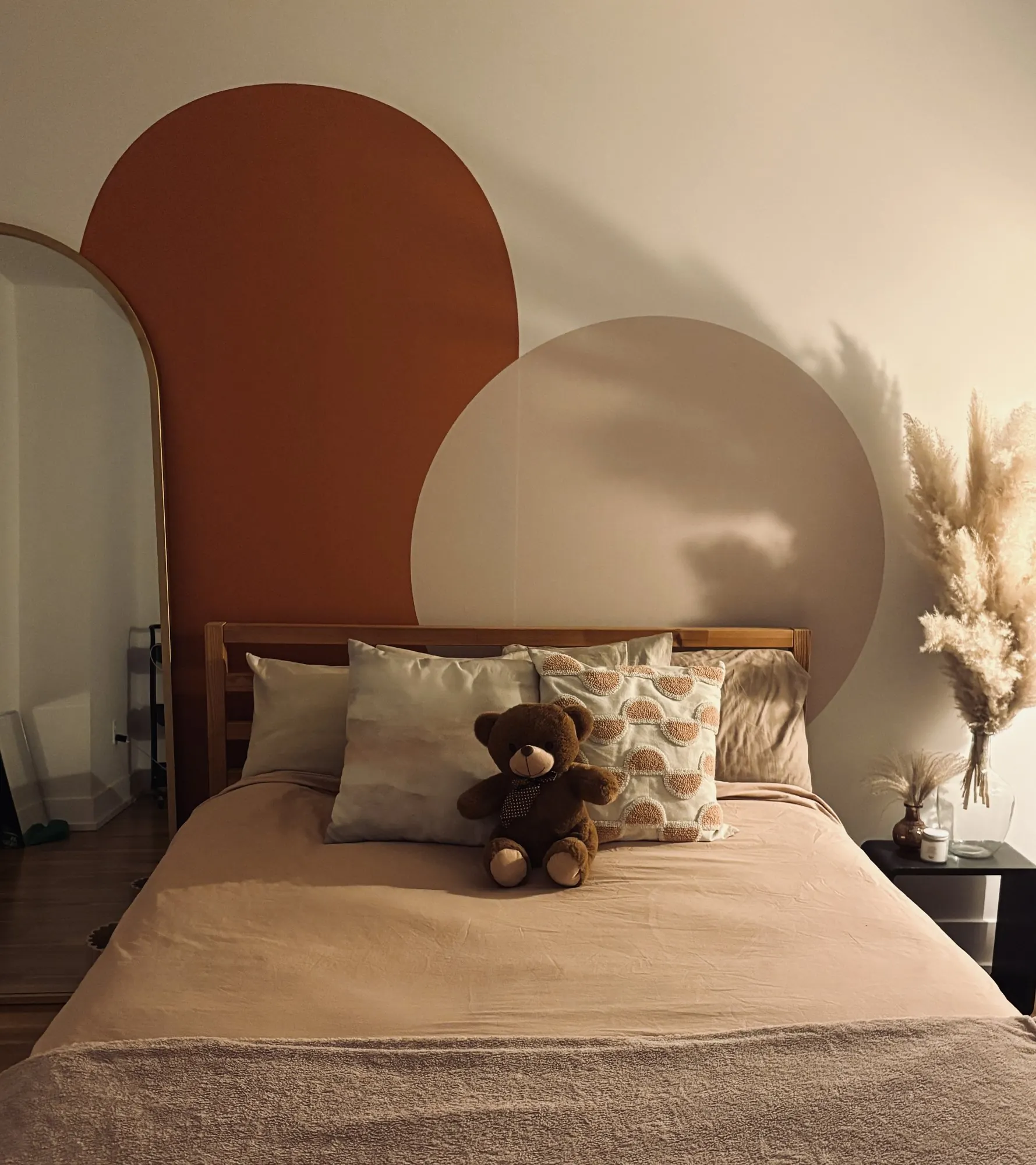 Murale aux arches terracotta et beige au-dessus d’un lit avec ourson en peluche
